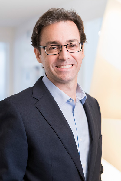 9431-2 Retrato de un hombre sonriente con gafas y traje oscuro posando en un entorno profesional iluminado con luz natural.